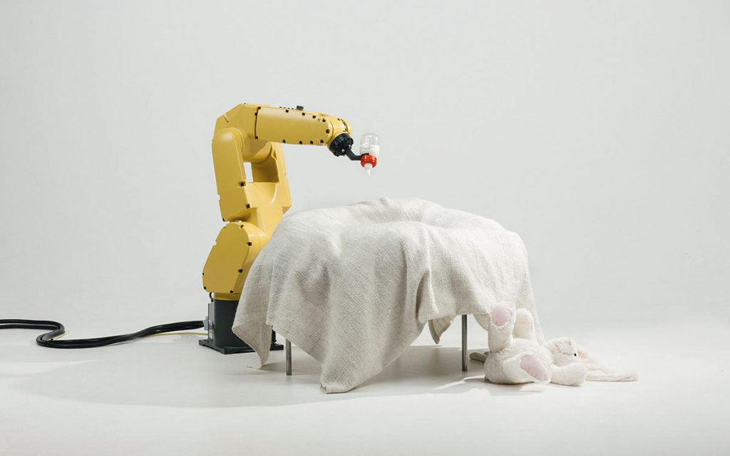 A robot arm holding a baby bottle over a crib.