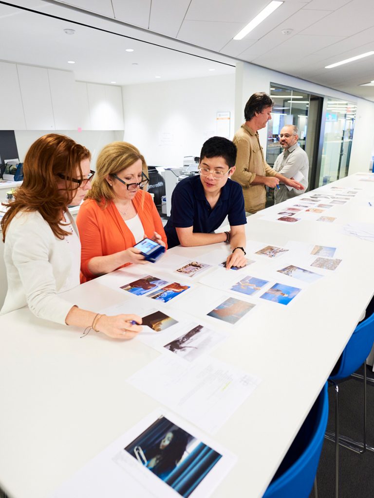 A group of people sitting at a long white table looking at photographs.
