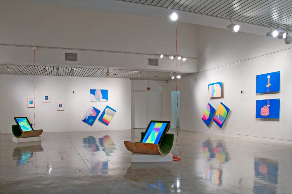 A gallery view with four wall paintings and a screen resting on a chair in front of the wall.
