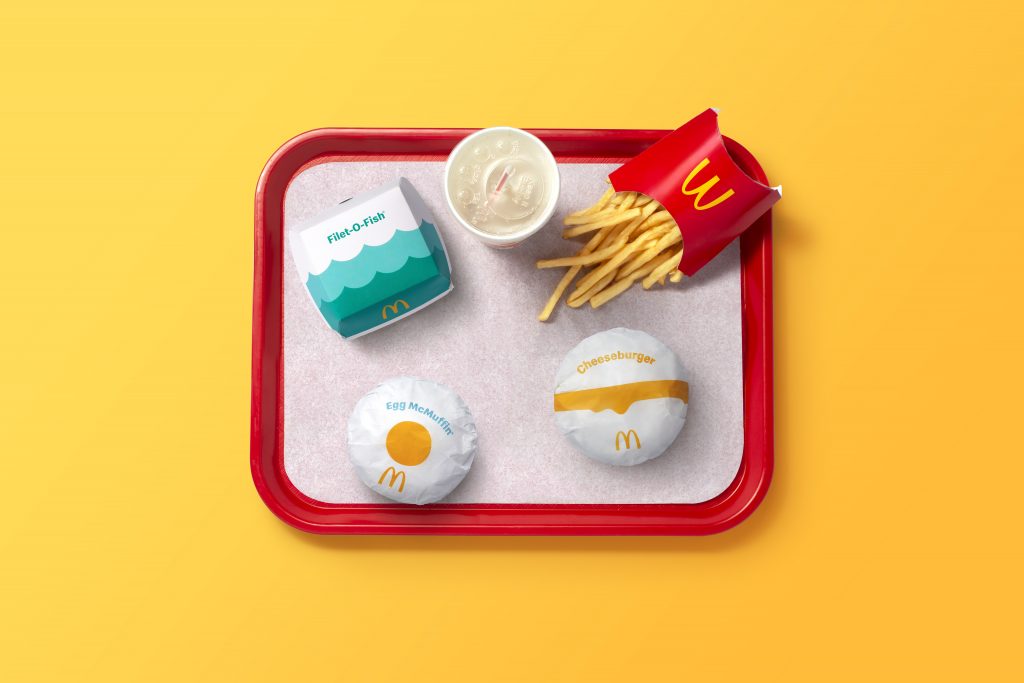 A McDonald’s burger, fries, chicken fingers and drink on a red tray with a yellow background.