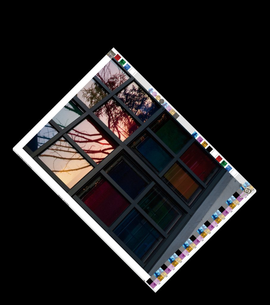 A book lying on a patterned rug. The book’s cover is a photograph of a window and some trees, and it looks reflective, like glass.
