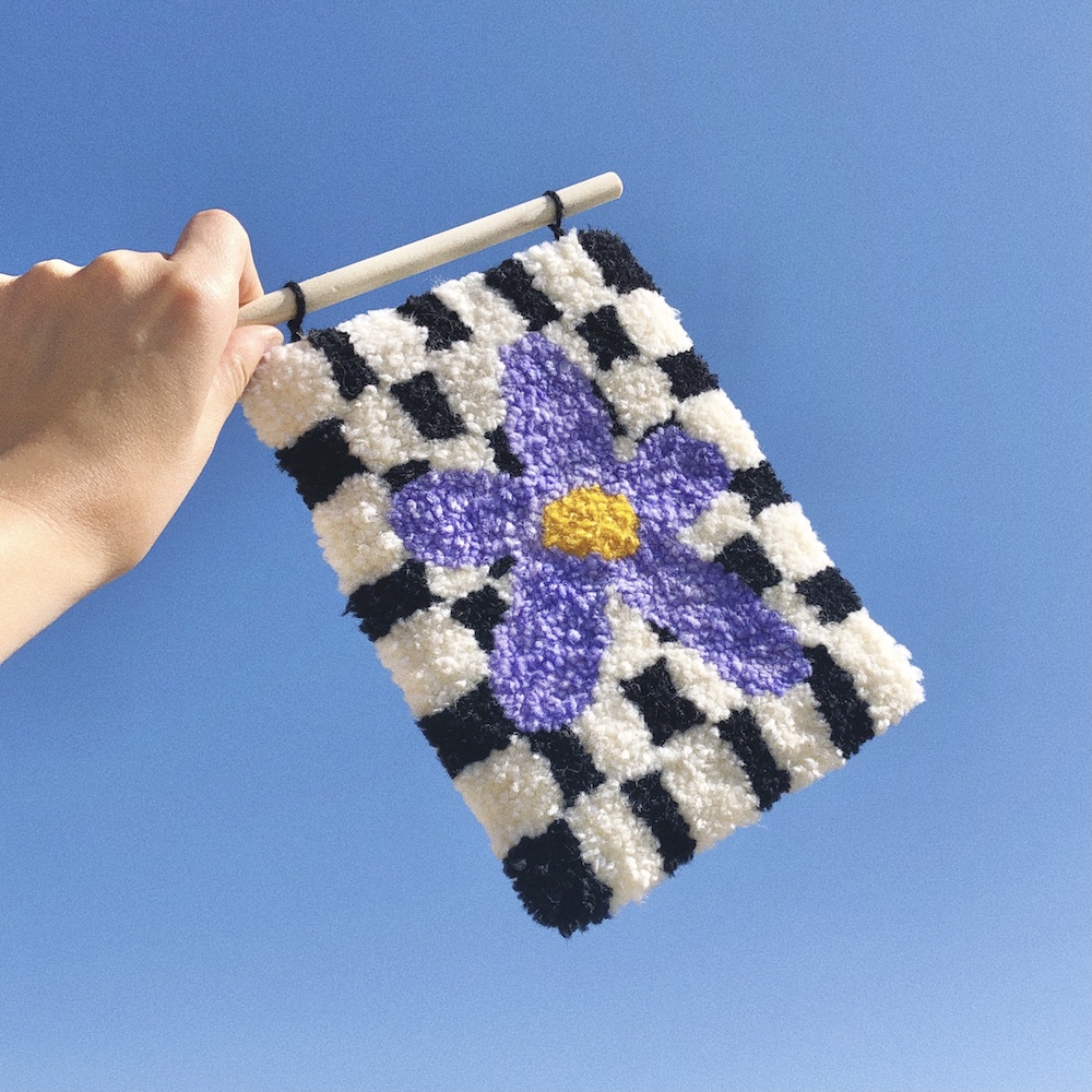 Hand holding a small tufted rug against a blue sky